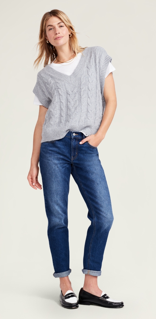 Une femme vêtue d’un jean Boyfriend foncé à coupe décontractée, un gilet en tricot côtelé ample et un t-shirt.