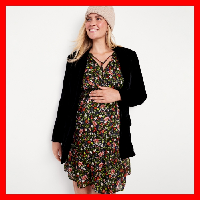 A maternity model wearing a Waist-Defined Floral Shine Mini Dress with black cardigan sweater