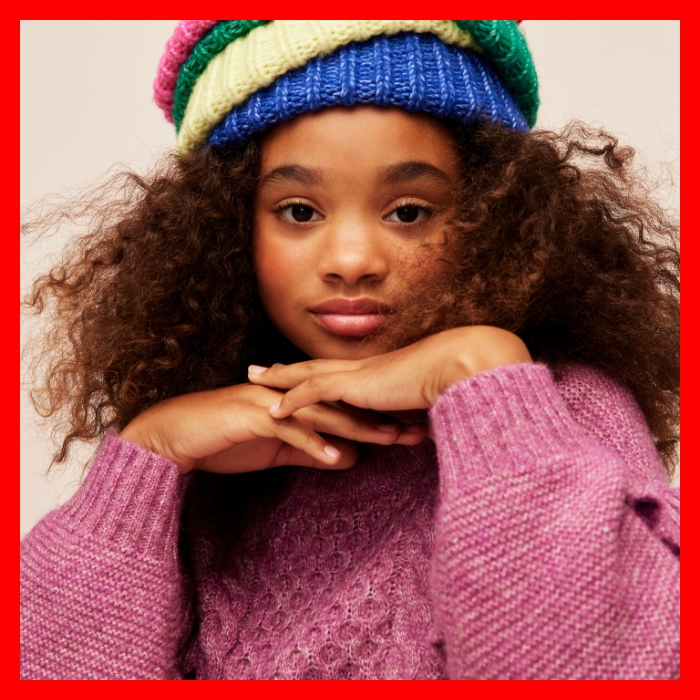 A young girl in a fuscia sweater and stacked colorful beanies.