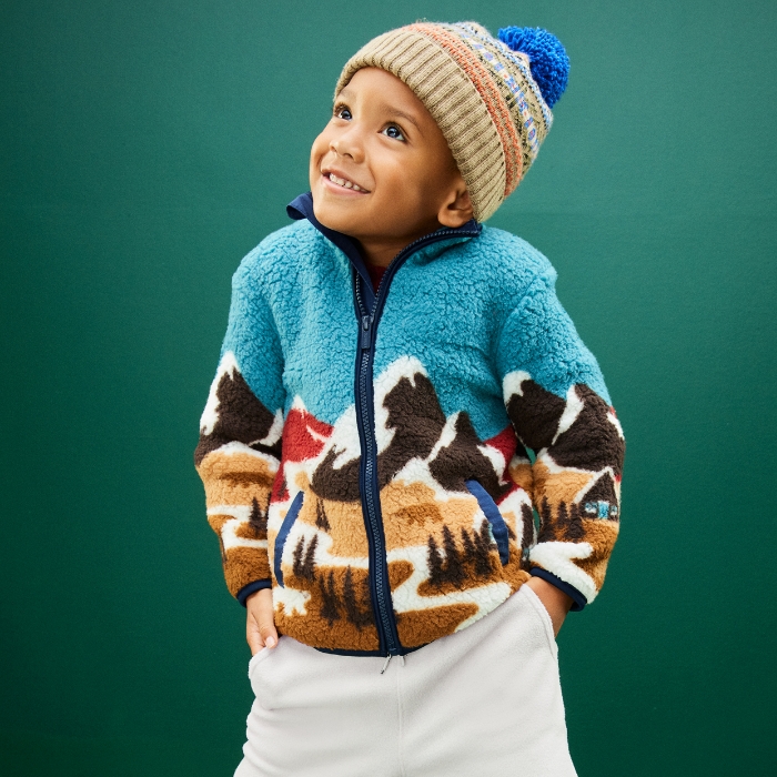 A toddler boy dressed in a cozy jacket jacket, sweatpants, and a beanie.