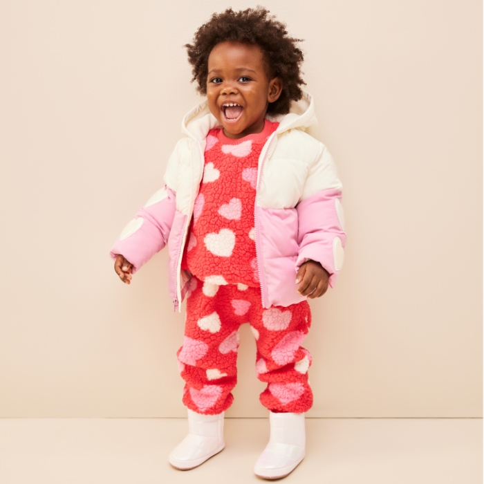 A baby girl dressed in unisex printed sherpa top and jogger pants set and a jacket.