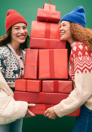 Two female models wearing Fair Isle sweaters holding stack of red wrapped gifts.