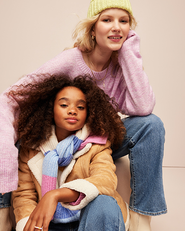 A woman and her daughter in soft neutral color sweaters and blue jeans.