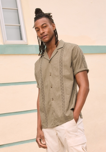 A male model wearing olive green short sleeve button down shirt and khaki shorts.