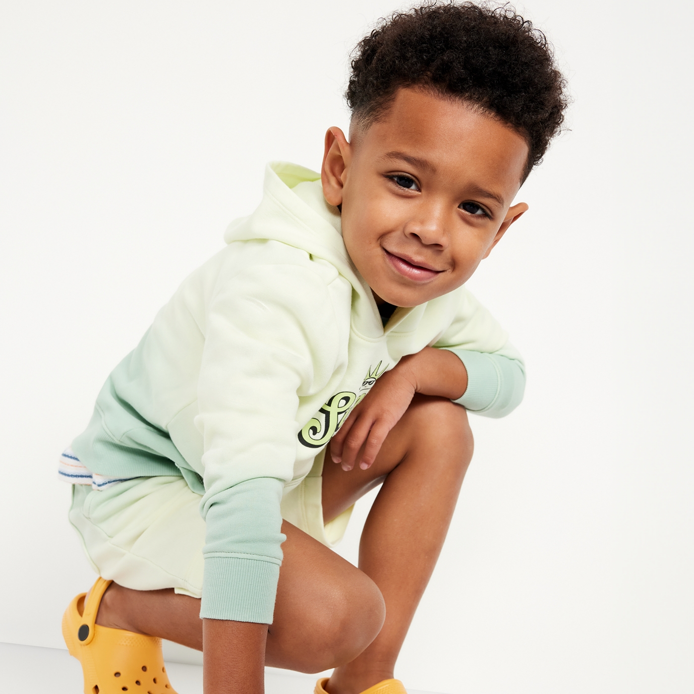 A toddler boy dressed head to toe in fleece sweatshirt and shorts.