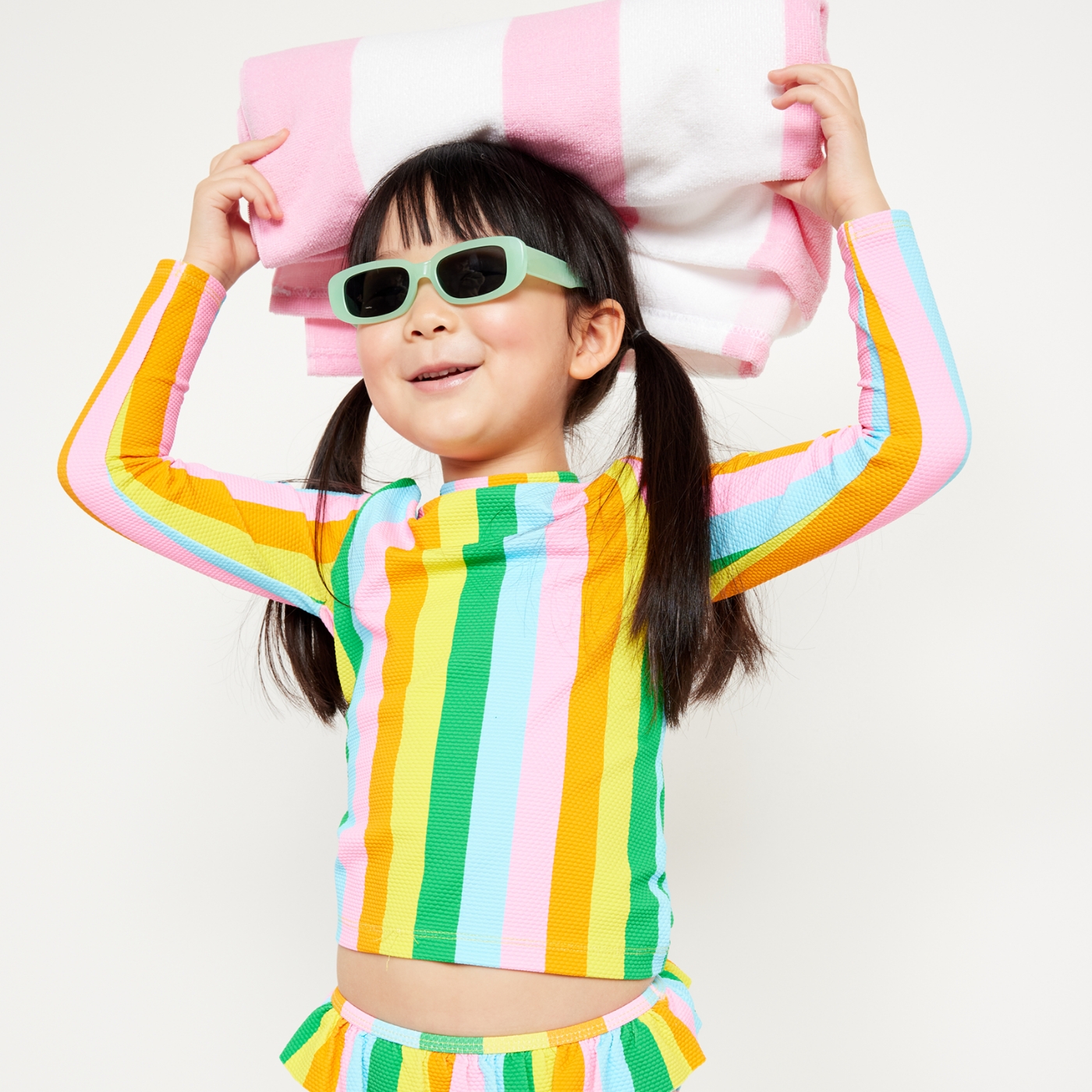 A toddler girl dressed in a matching rainbow stripe bathing suit.