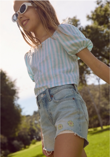 Young girl model wearing stripe shirt and jean shorts.