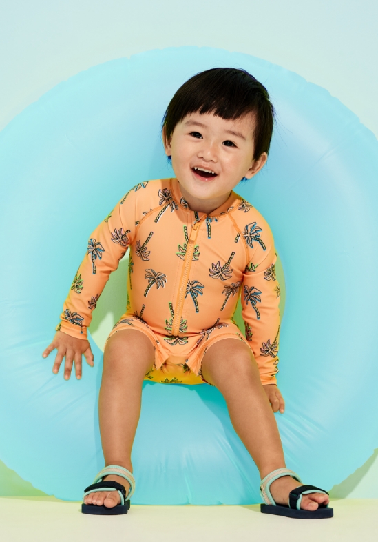 Young model wearing orange unisex long-sleeve swim rashguard bodysuit for baby.